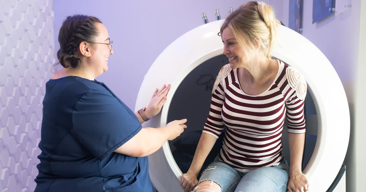 Client sitting in the OxyHealth Fortius 420 hard-shell hyperbaric chamber with a provider at iCRYO Daniel Island in Charleston, SC